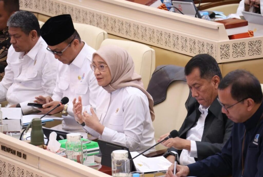 Menteri pendayagunaan aparatur negara dan reformasi birokrasi catrawarta Woman in a beige hijab speaks into a microphone at a formal meeting flanked by colleagues reviewing documents
